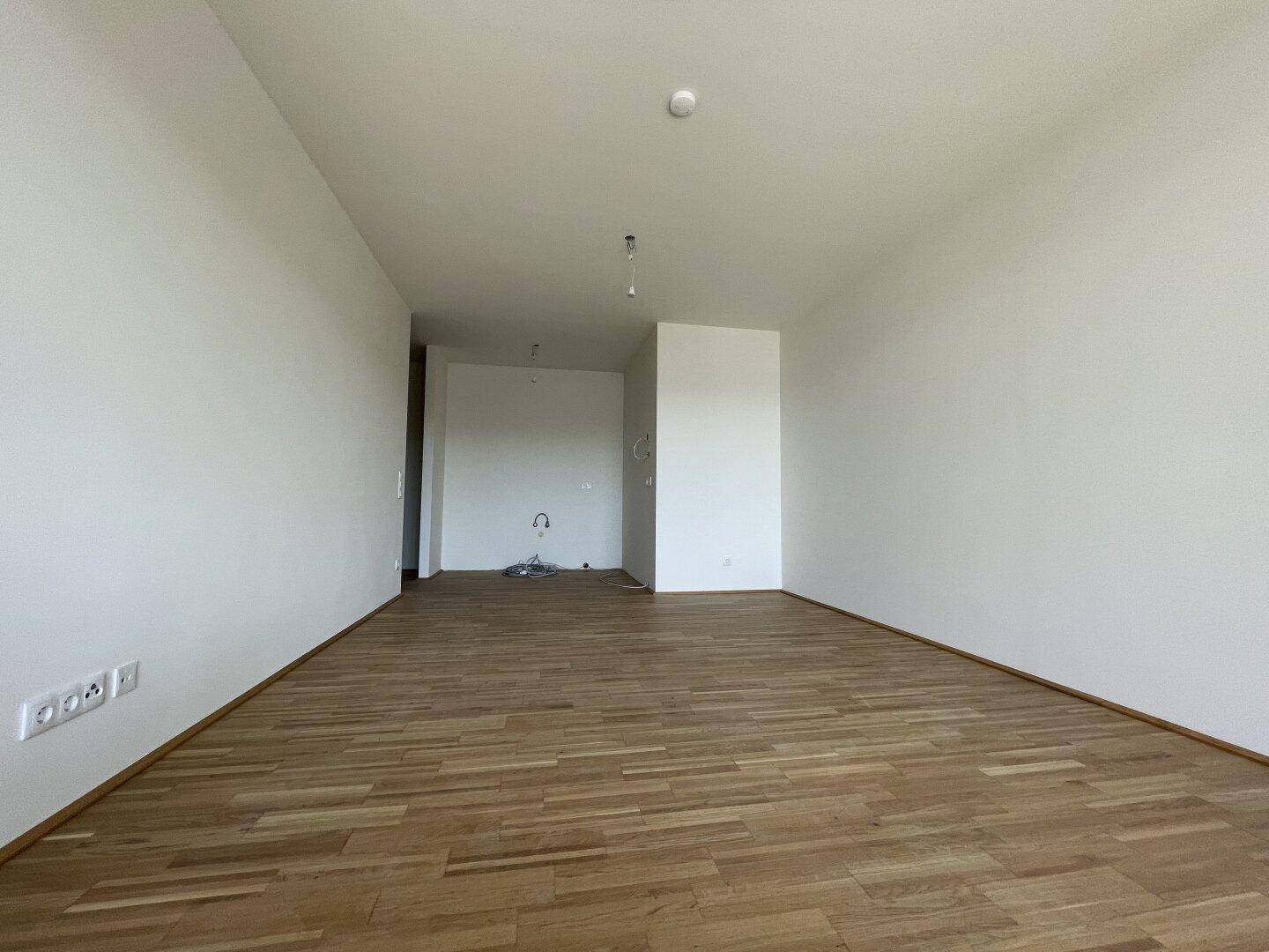 Geräumiger, heller Wohnbereich mit Parkettboden und weißen Wänden, bereit zur individuellen Gestaltung.
