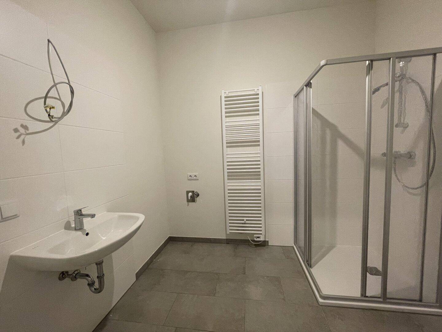 Modernes Badezimmer mit Dusche, Waschbecken und Handtuchheizkörper, in hellen Fliesen gehalten.