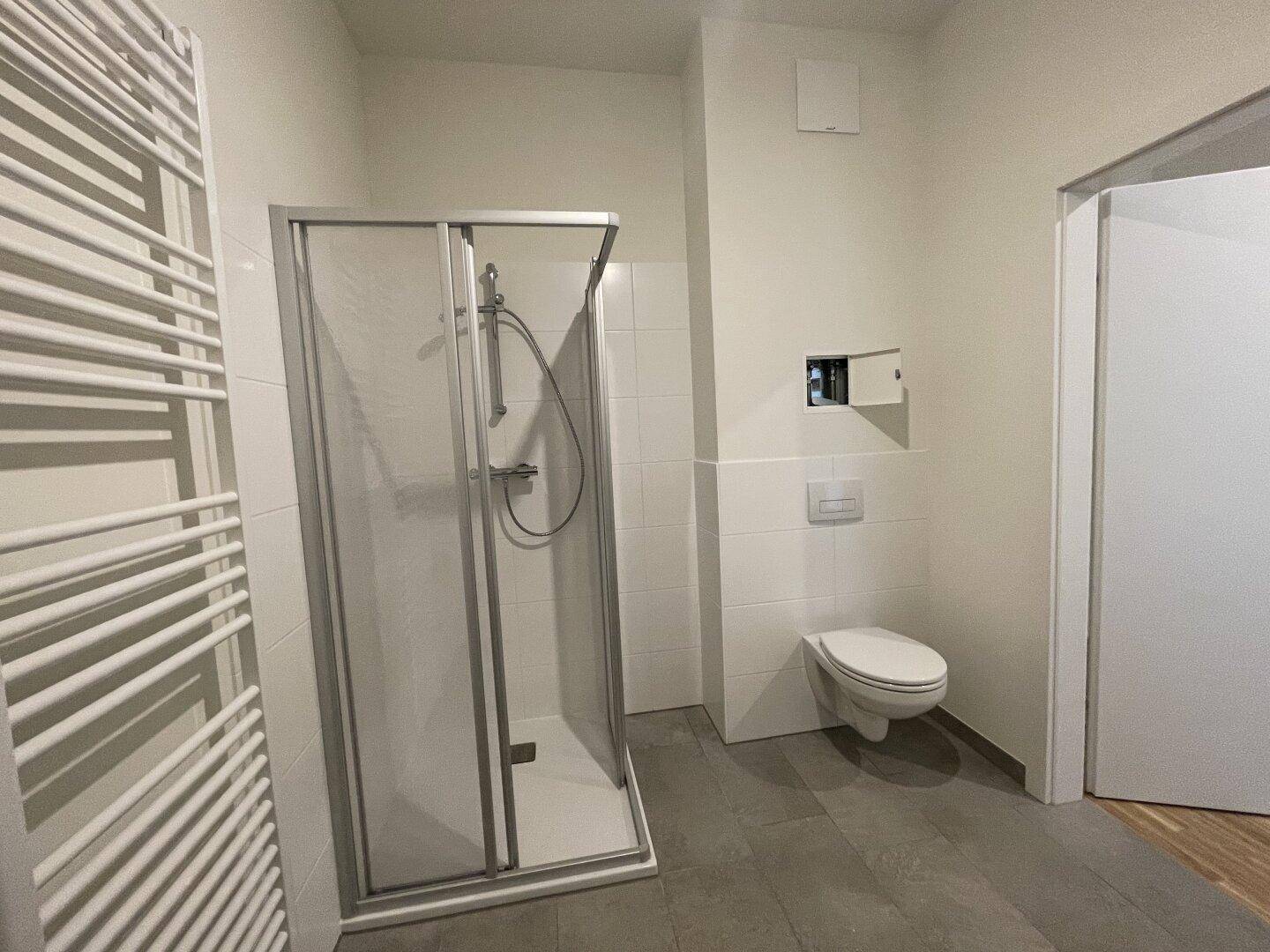 Zeitgemäßes Badezimmer mit Dusche und wandhängendem WC, ausgestattet mit einem Handtuchheizkörper.