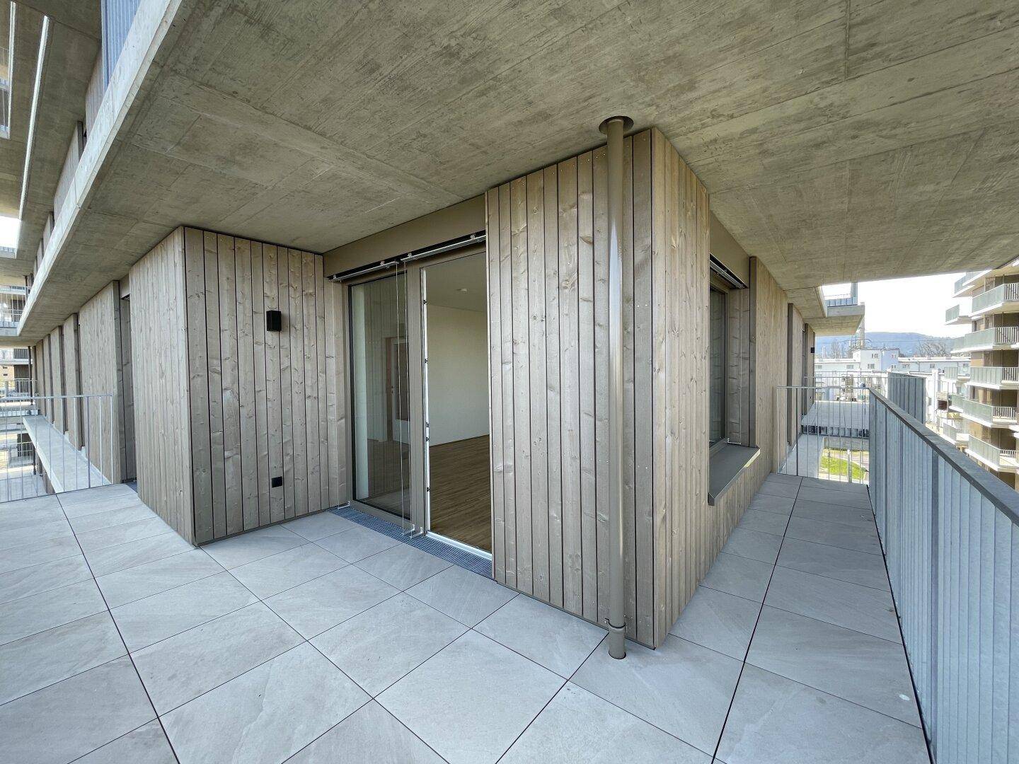 Großer Balkon mit Holzverkleidung an der Fassade und Zugang zu den Innenräumen.