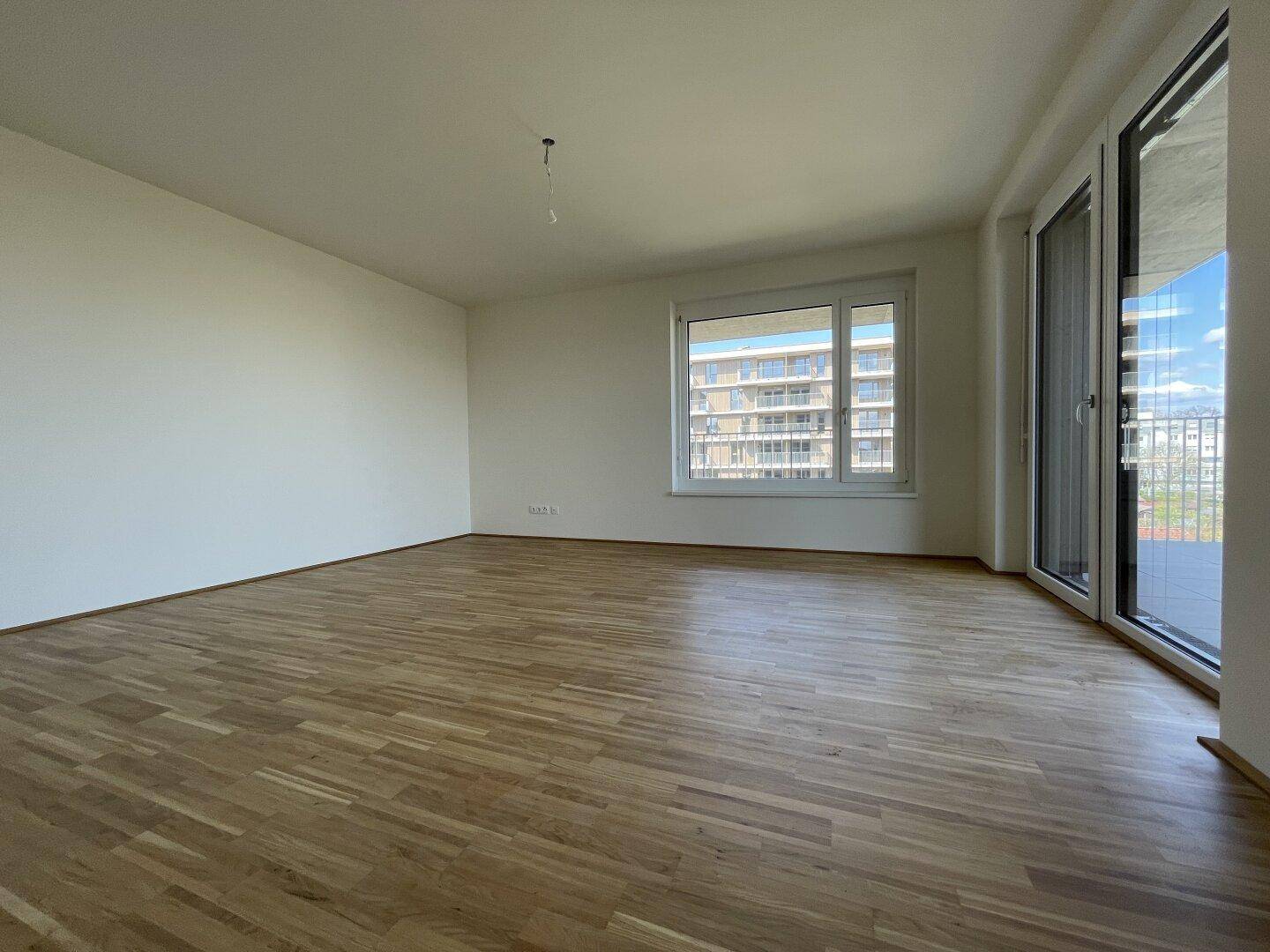 Helles, leeres Zimmer mit Parkettboden und großen Fenstern, bereit zur individuellen Gestaltung.