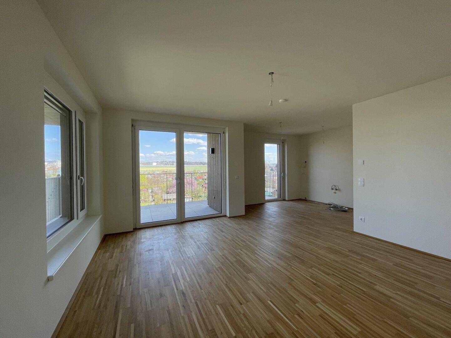 Geräumiger, heller Raum mit Parkettboden und Zugang zu einem Balkon, ideal für Wohn-Essbereich.