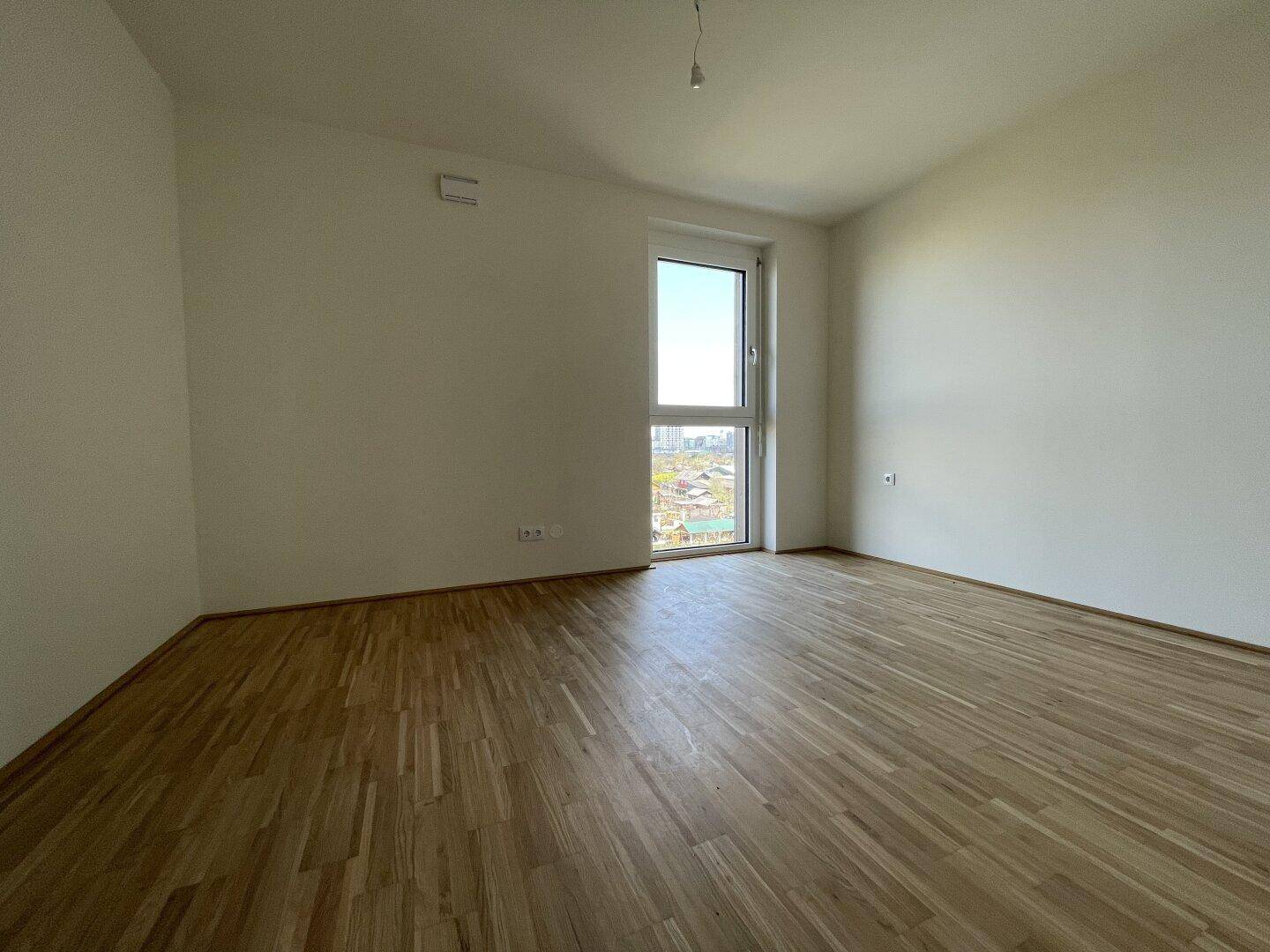 Helles Schlafzimmer mit Parkettboden und großem Fenster, bietet einen angenehmen Ausblick.