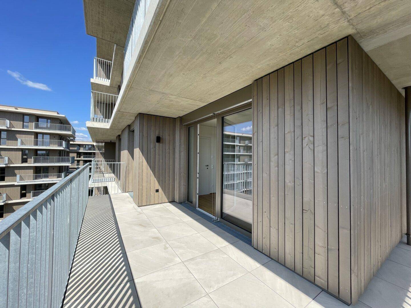 Geräumiger Balkon mit Holzverkleidung, Fliesenboden und Zugang zu den Innenräumen.