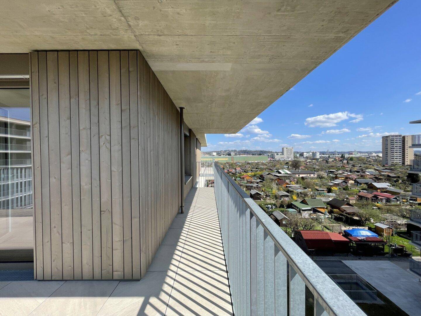 Langer Balkon mit weitem Blick über Kleingärten und die städtische Skyline in der Ferne.