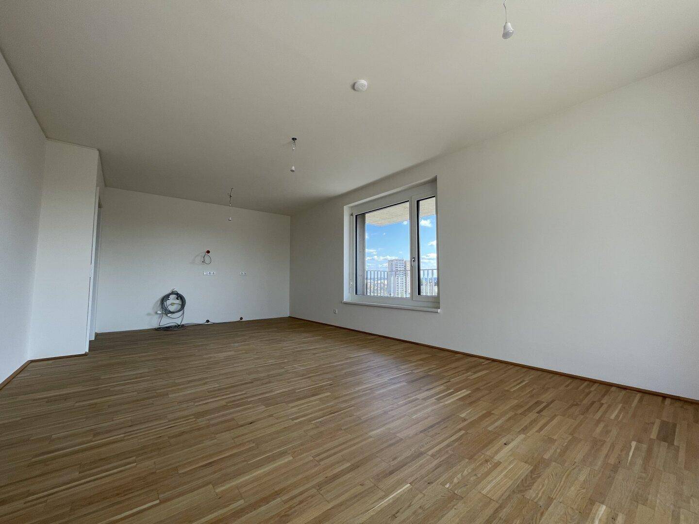Geräumiges, helles Wohnzimmer mit Holzboden und großem Fenster, bereit für die Einrichtung.