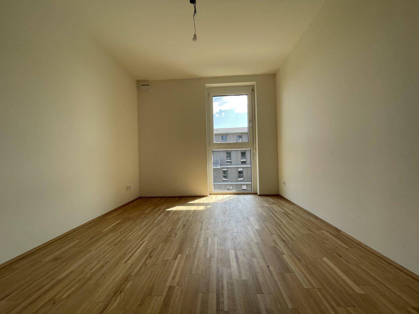 Helles Schlafzimmer mit Parkettboden und einem Fenster, das viel Tageslicht hereinlässt.