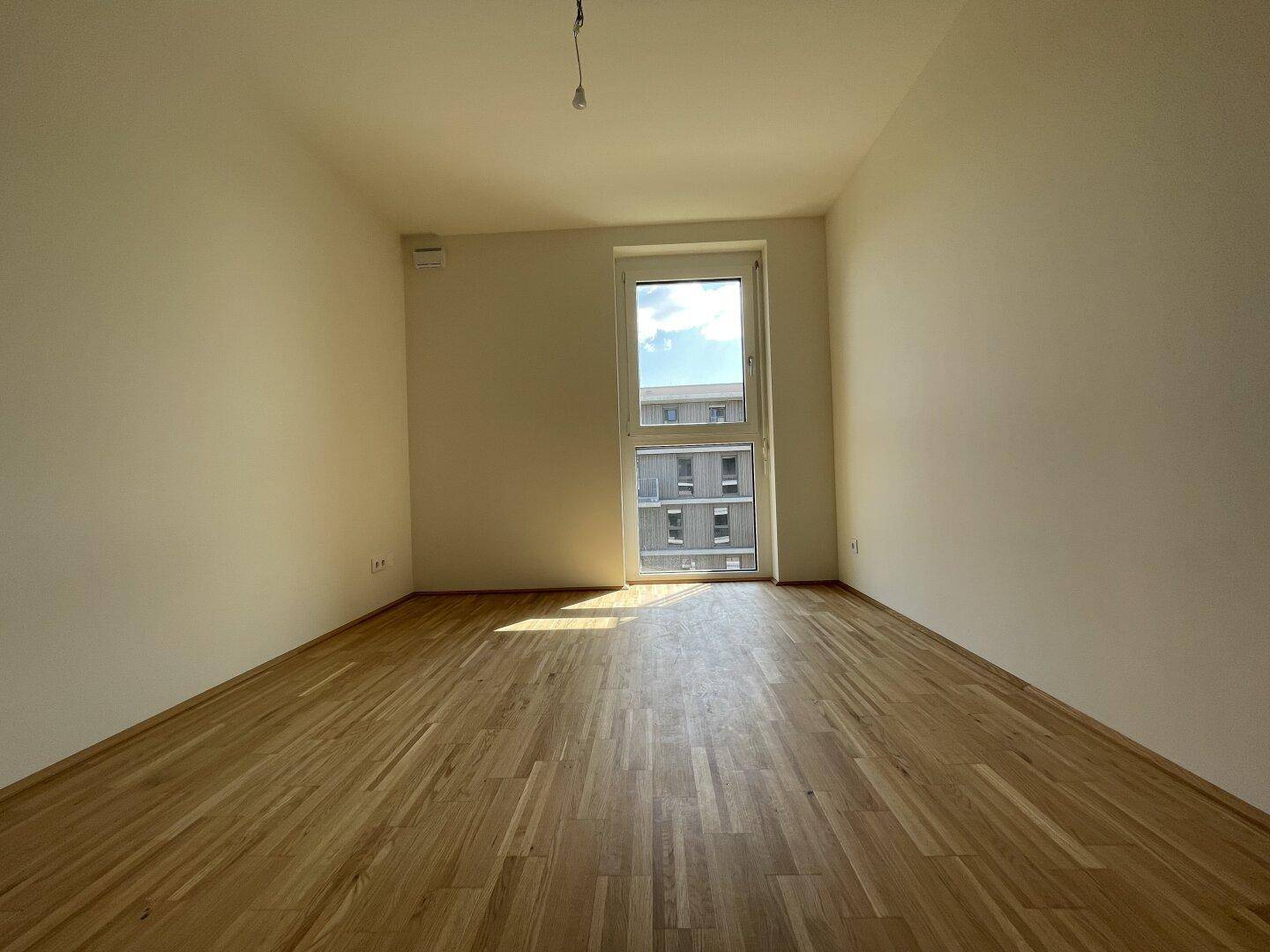 Freundliches Schlafzimmer mit Holzboden und einem Fenster, das eine angenehme Atmosphäre schafft.