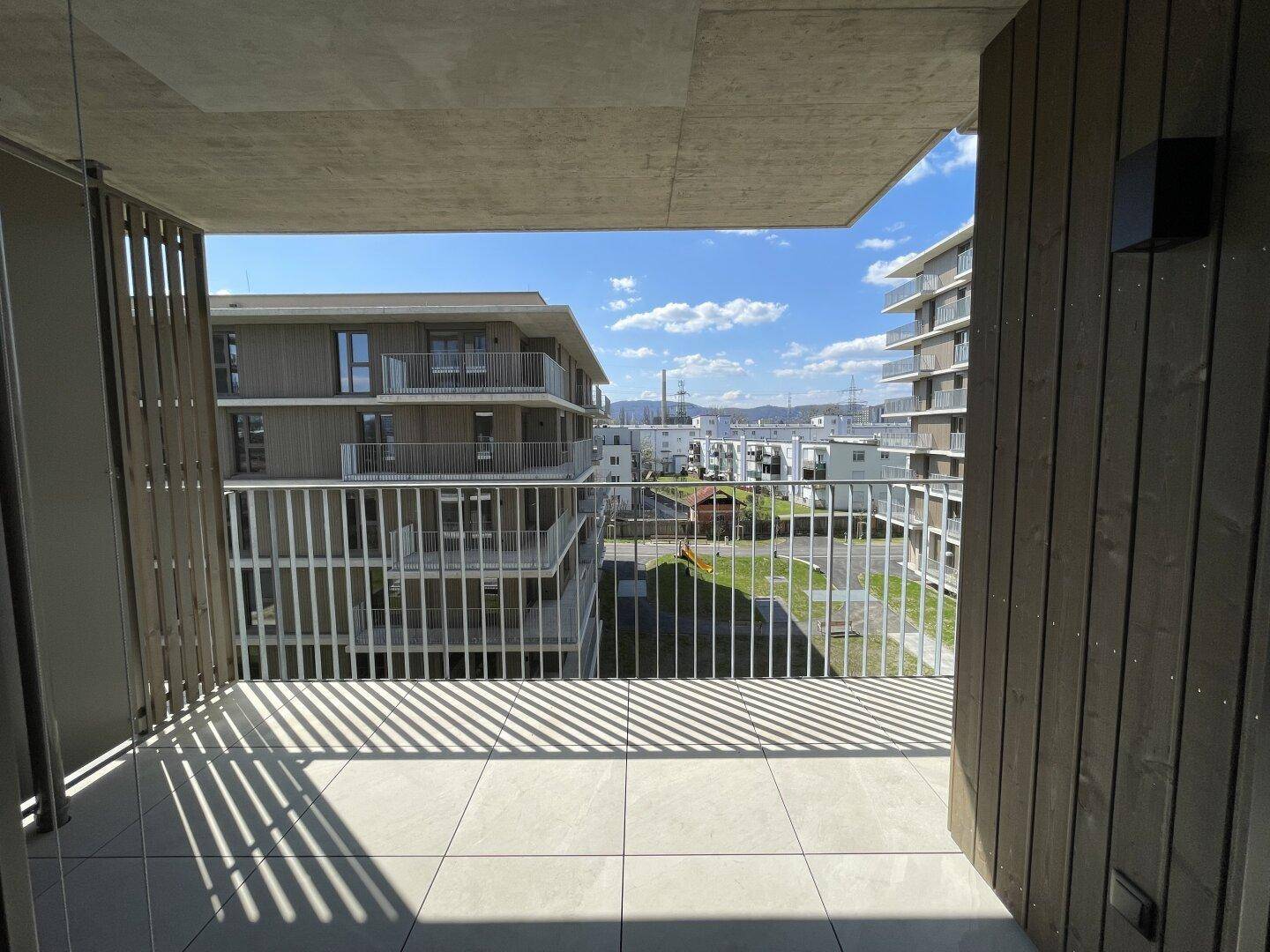 Heller Balkon mit Fliesenboden und Ausblick auf die Nachbargebäude und den Himmel.