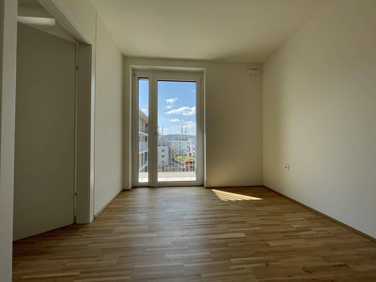 Lichtdurchflutetes Zimmer mit Parkettboden und großem Fenster mit Blick ins Grüne.