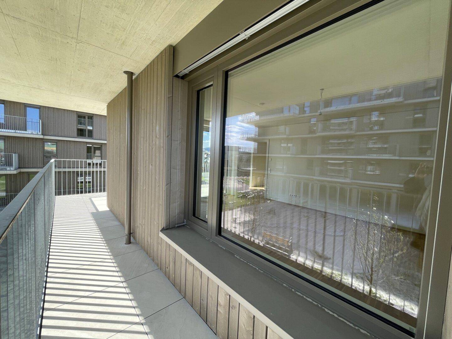 Langer Balkon mit Holzverkleidung und großem Fenster, das das Innere widerspiegelt.