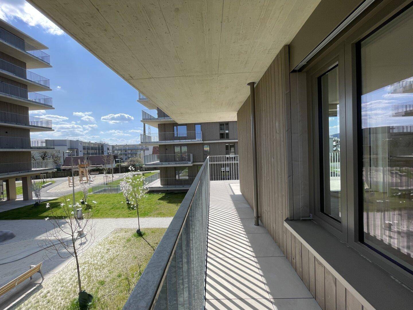 Sonniger Balkon mit Blick auf den begrünten Innenhof und die modernen Wohngebäude.