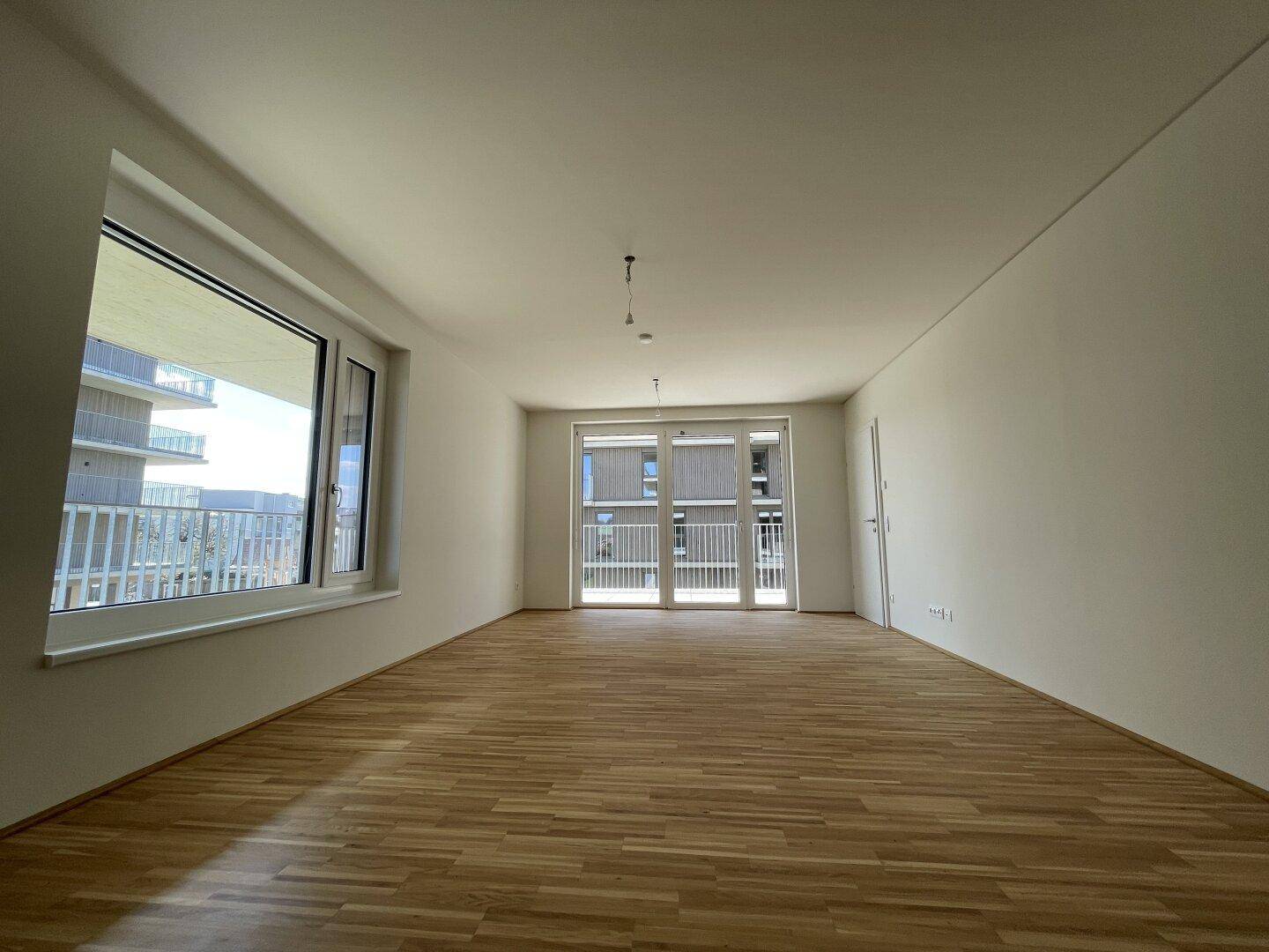 Helles, leeres Zimmer mit Parkettboden und Zugang zu einem französischen Balkon.