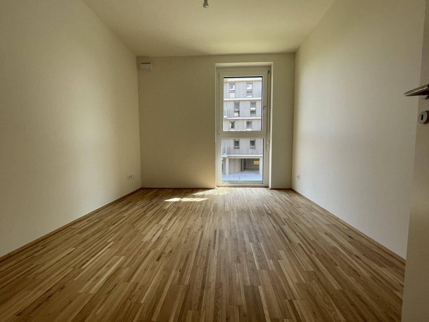 Ruhiges Schlafzimmer mit Parkettboden und hohem Fenster, das viel Licht hereinlässt.