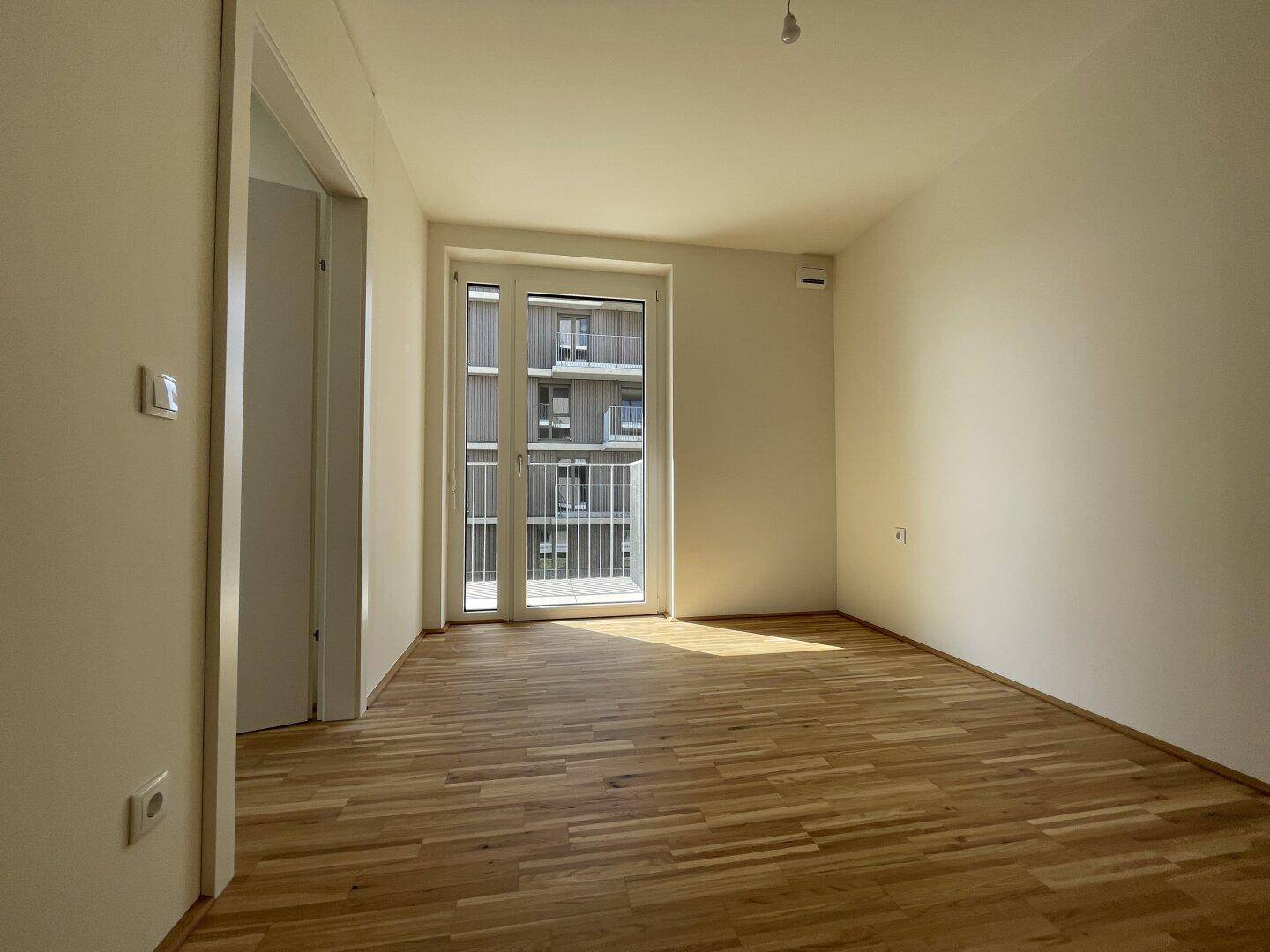 Helles Schlafzimmer mit Parkettboden und Zugang zu einem französischen Balkon.