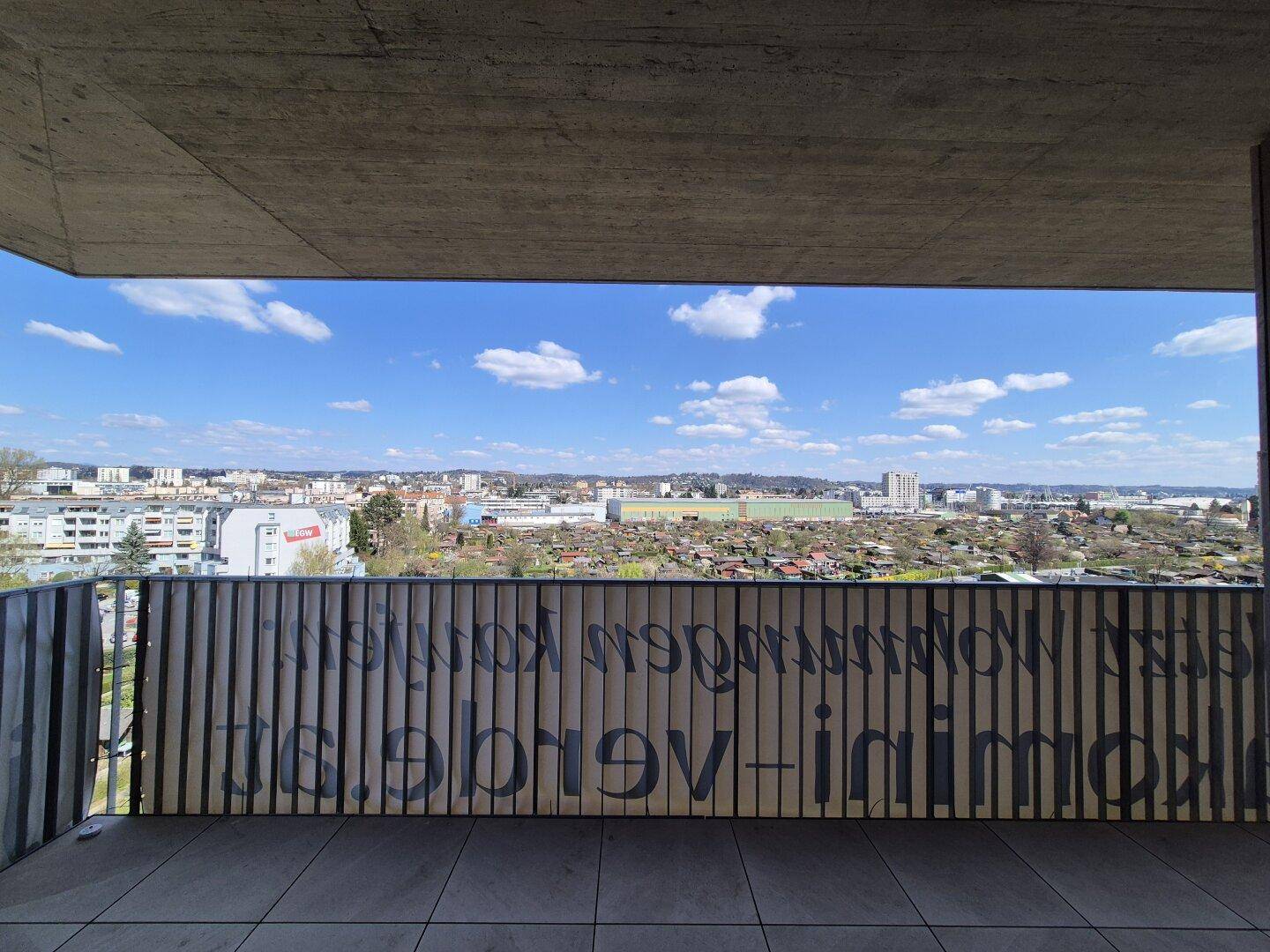 Balkon mit weitem Ausblick über die Stadt und Kleingärten unter blauem Himmel.