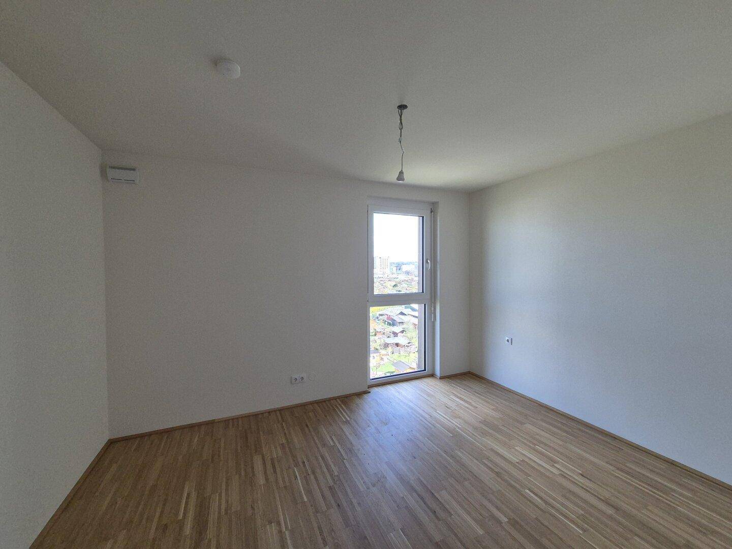 Leeres Zimmer mit Parkettboden und großem Fenster, ideal für Schlaf- oder Arbeitsbereich.
