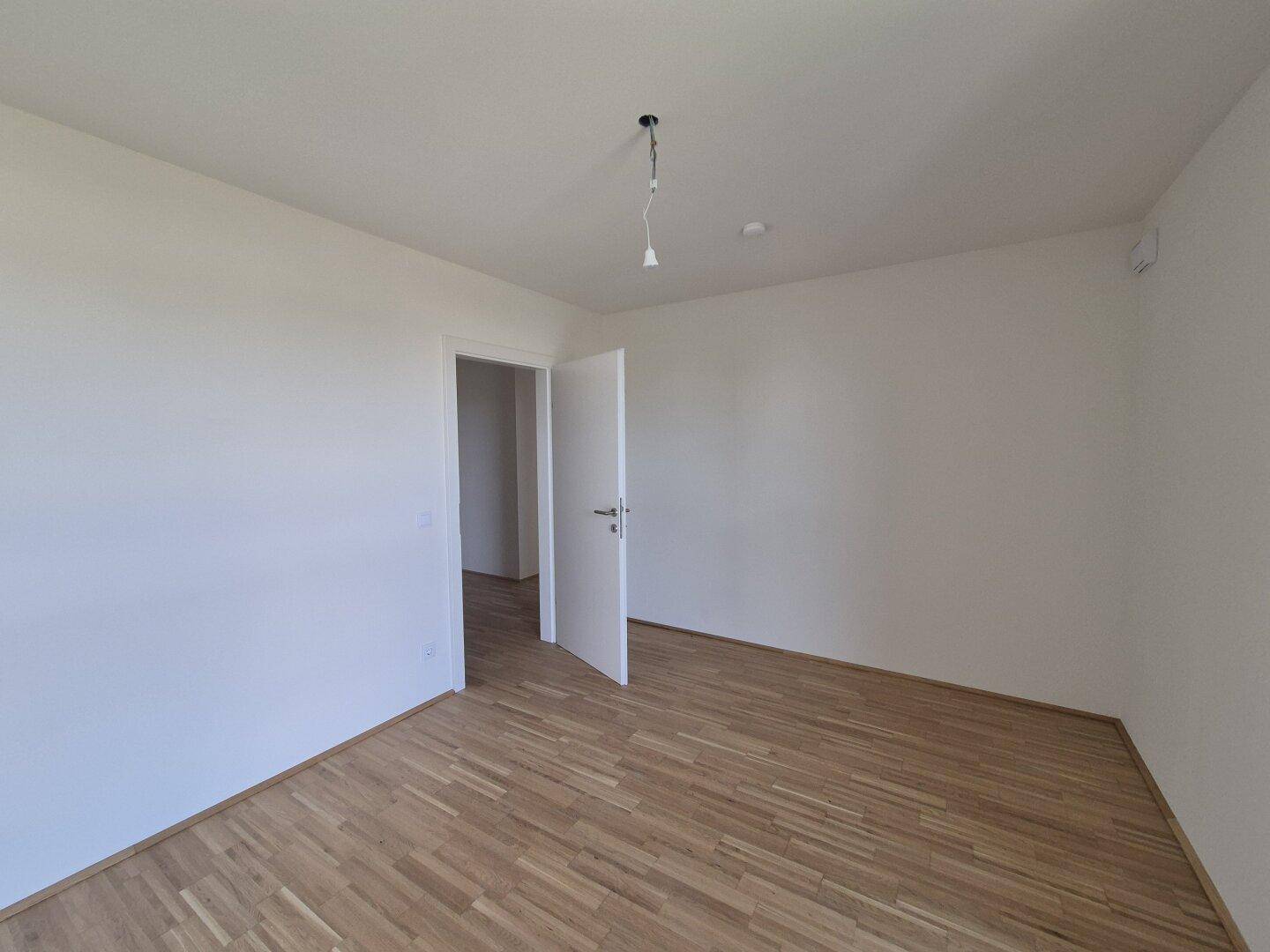 Geräumiges, helles Zimmer mit Parkettboden und Zugang zu weiteren Räumen.