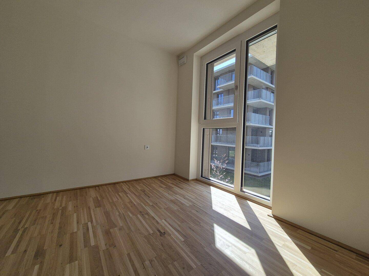 Sonniges Schlafzimmer mit Parkettboden und Blick auf die umliegenden Gebäude.