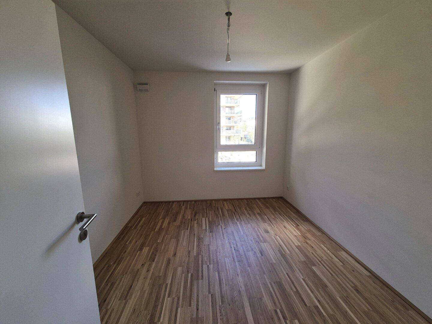 Kleineres Schlafzimmer mit Parkettboden und einem Fenster, das den Raum erhellt.