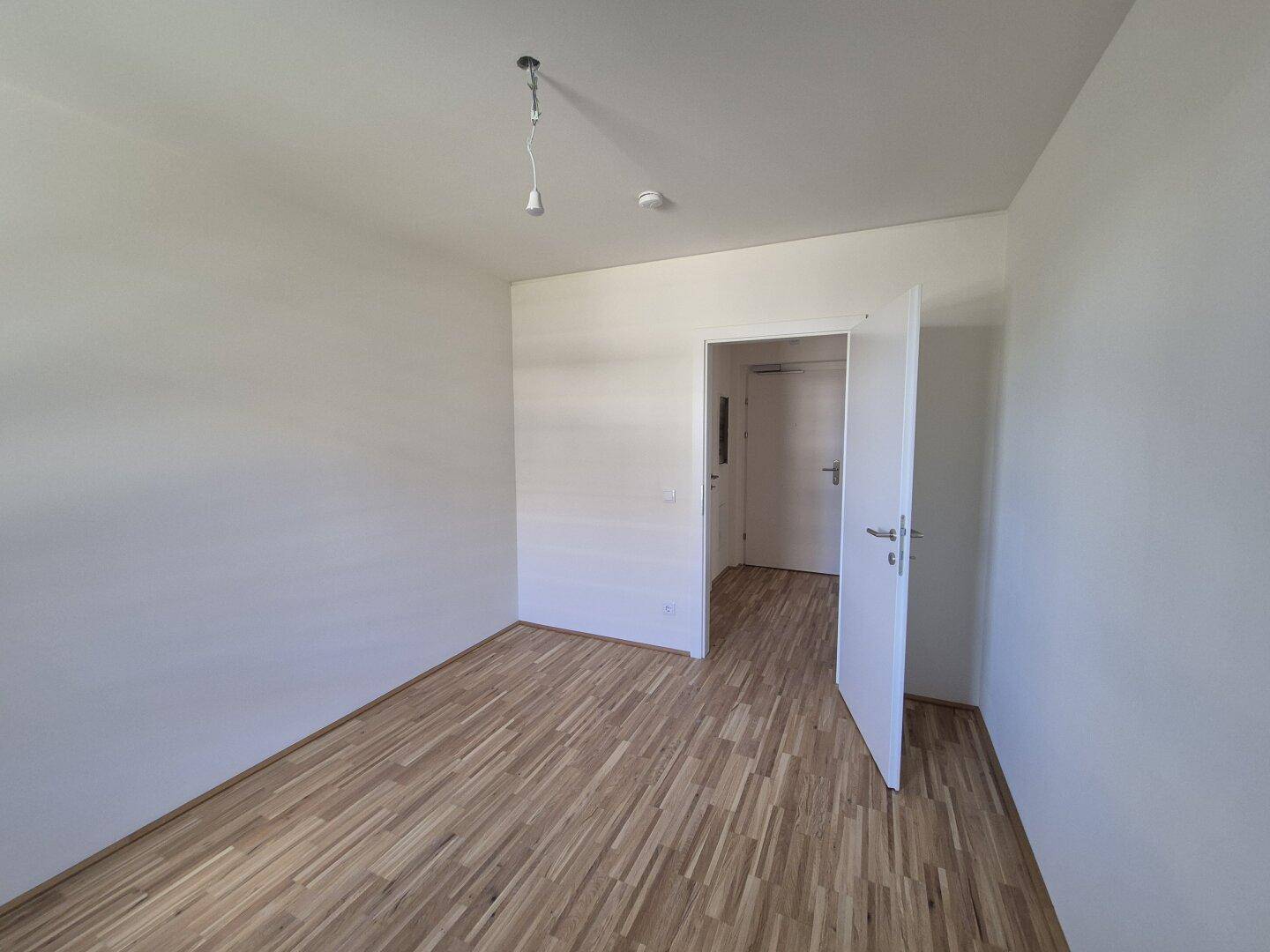 Leeres Schlafzimmer mit Parkettboden und weiß gestrichenen Wänden, bereit zum Einzug.