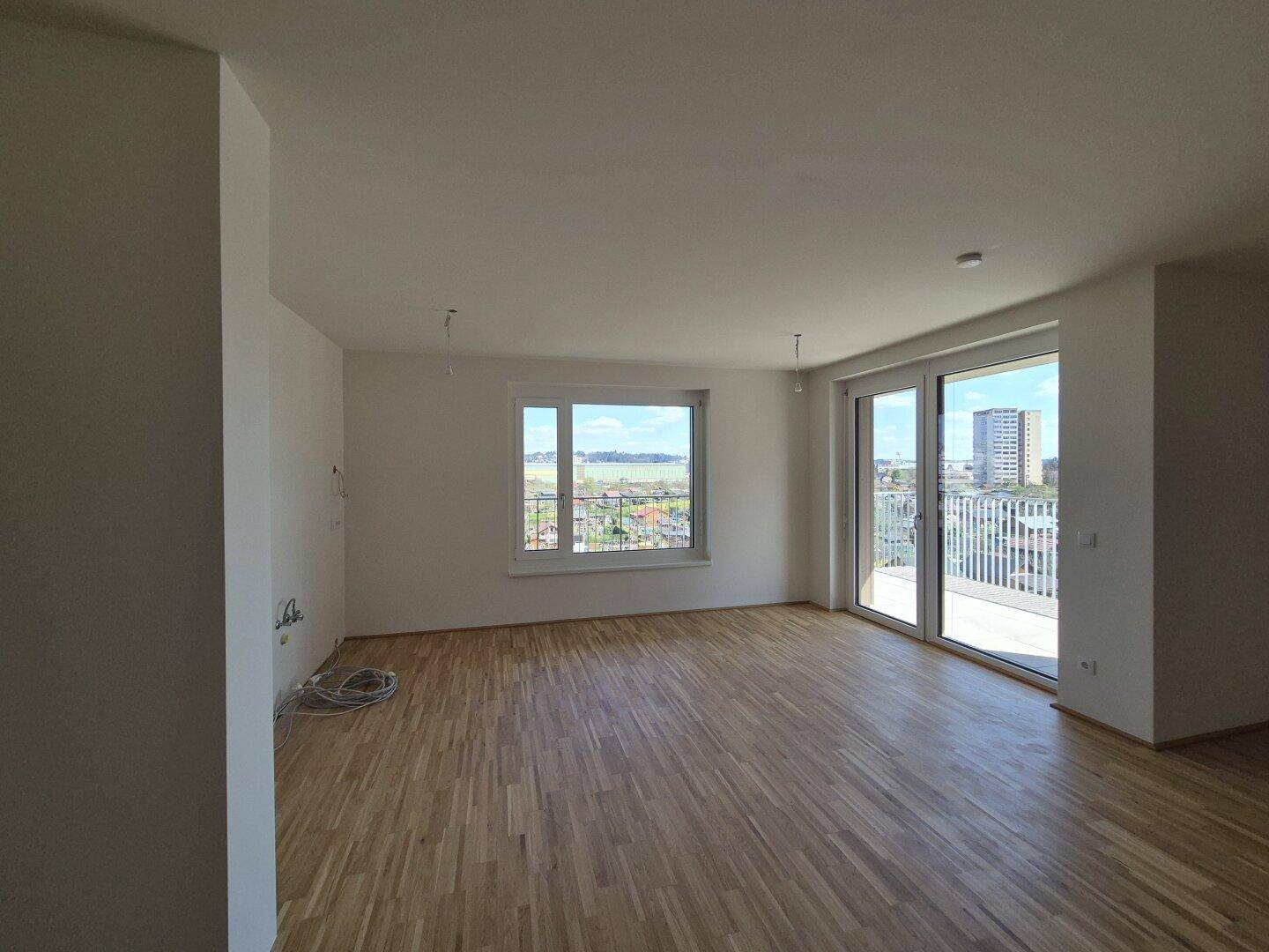 Geräumiges, helles Wohnzimmer mit Holzboden und großen Fenstern, die viel Tageslicht hereinlassen.