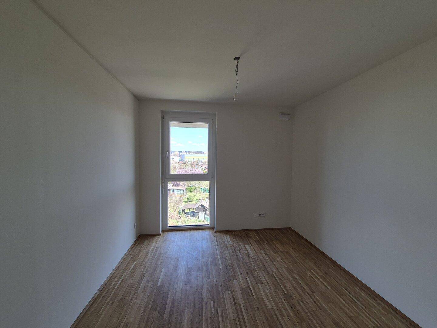 Helles Schlafzimmer mit Parkettboden und einem großen Fenster, das viel Tageslicht bietet.