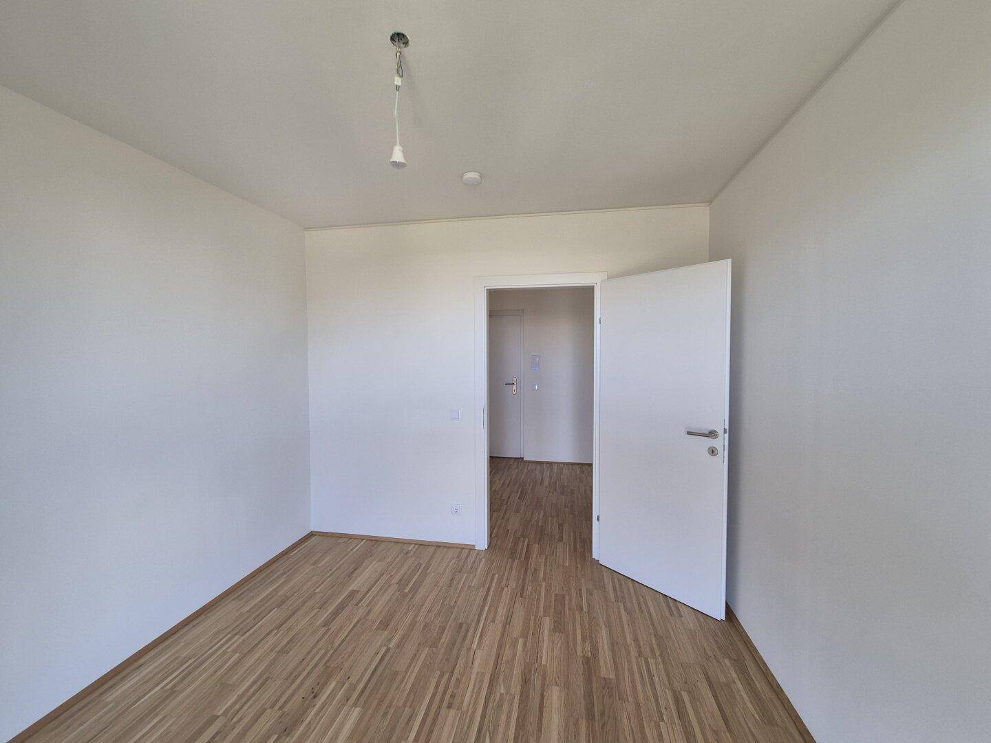 Leeres Schlafzimmer mit Parkettboden und weiß gestrichenen Wänden, bereit zur individuellen Gestaltung.