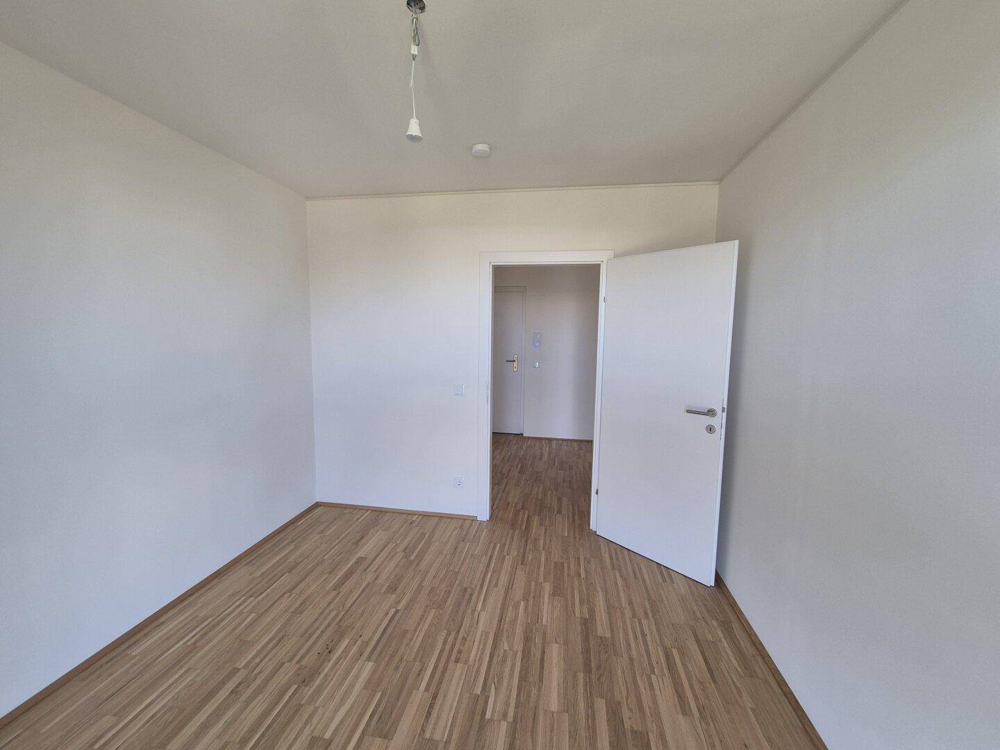 Geräumiges Schlafzimmer mit hellem Parkettboden und einer Tür, die zu einem weiteren Raum führt.