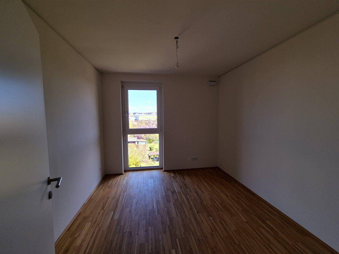 Leeres Zimmer mit Parkettboden und weiß gestrichenen Wänden, ideal als Schlaf- oder Arbeitszimmer.