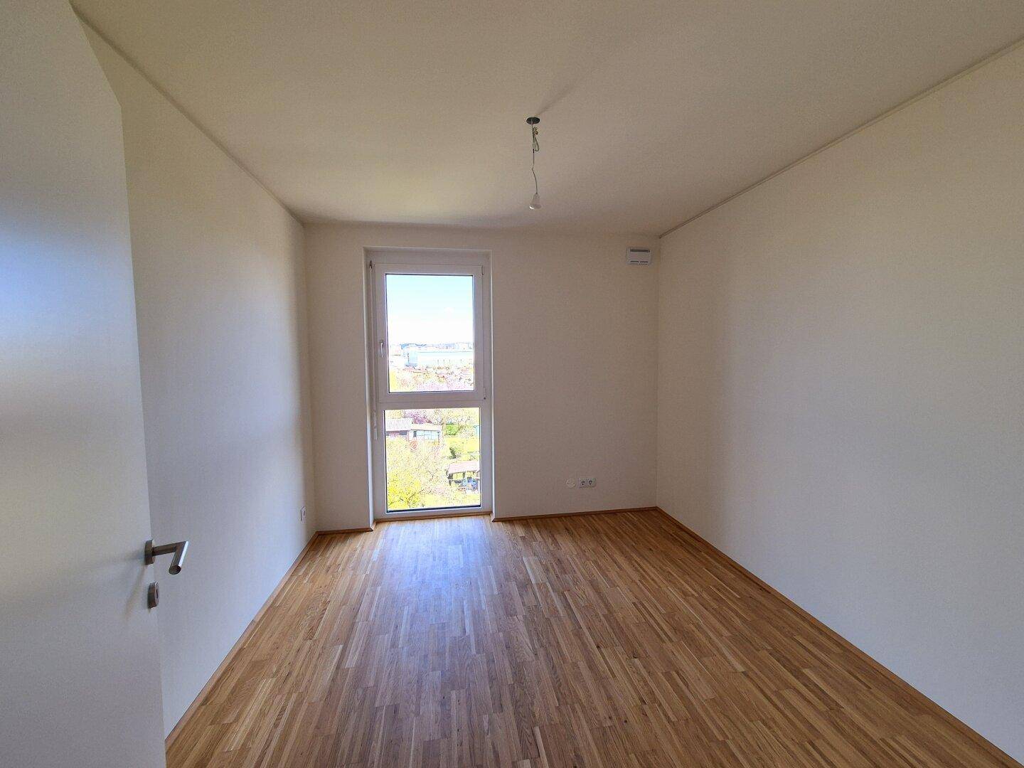 Helles Zimmer mit Parkettboden und einem Fenster, das viel Tageslicht in den Raum bringt.