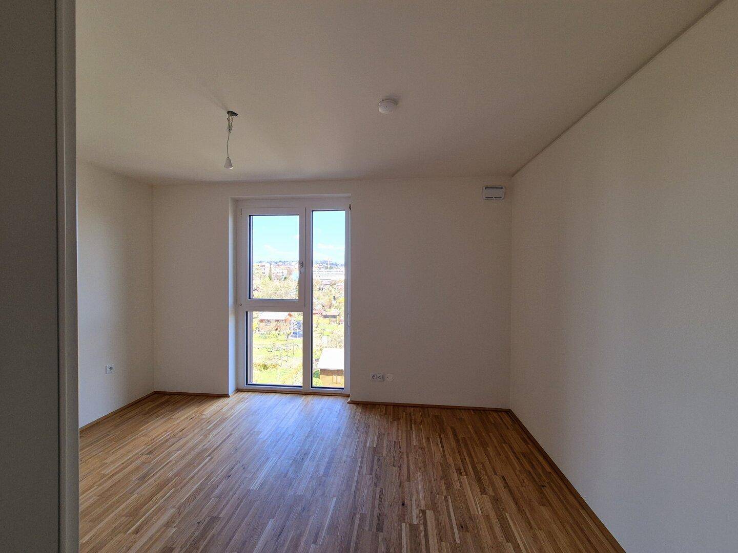 Helles Schlafzimmer mit Parkettboden und Zugang zu einem Balkon, der einen weiten Blick bietet.