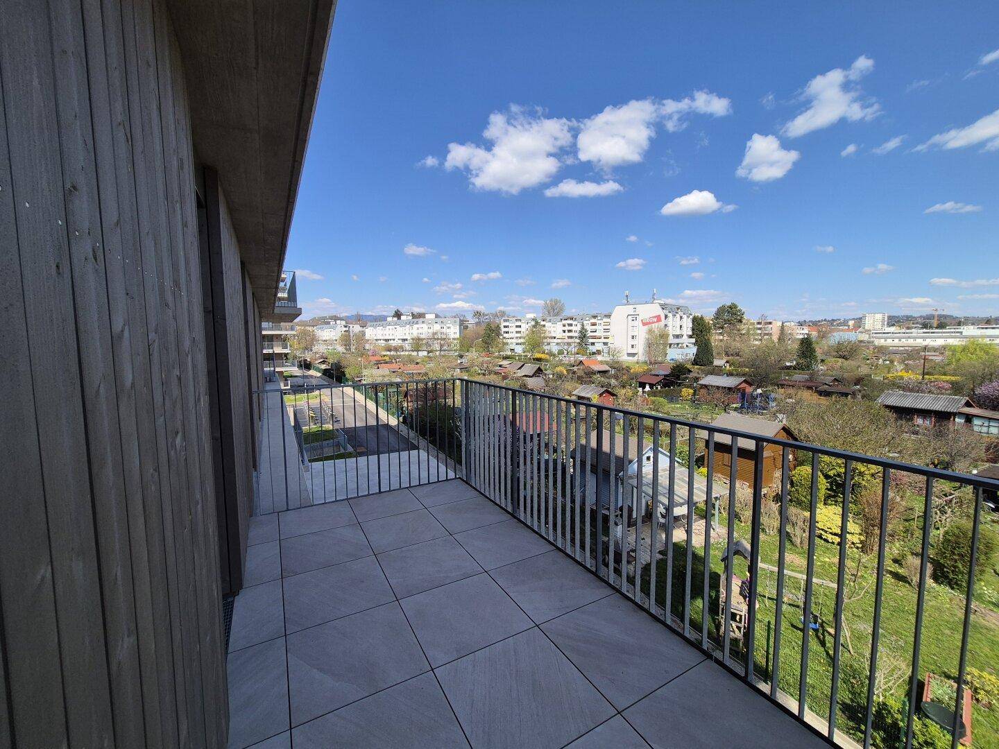 Geräumiger Balkon mit Fliesenboden und weitem Blick über grüne Schrebergärten und die Stadt.