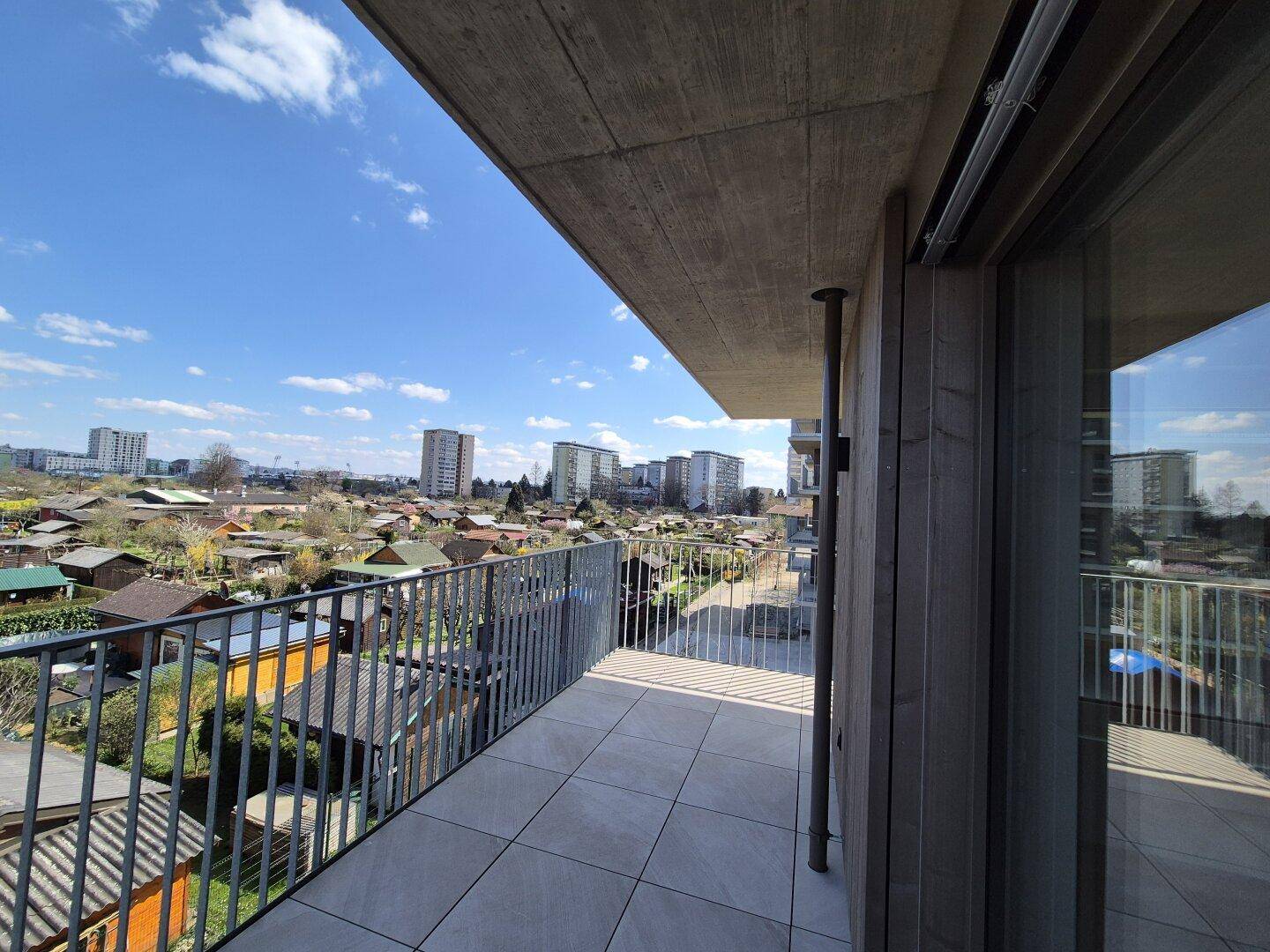 Moderner Balkon mit Betonüberdachung, Holzverkleidung und Panoramablick über die Stadt und Gärten.
