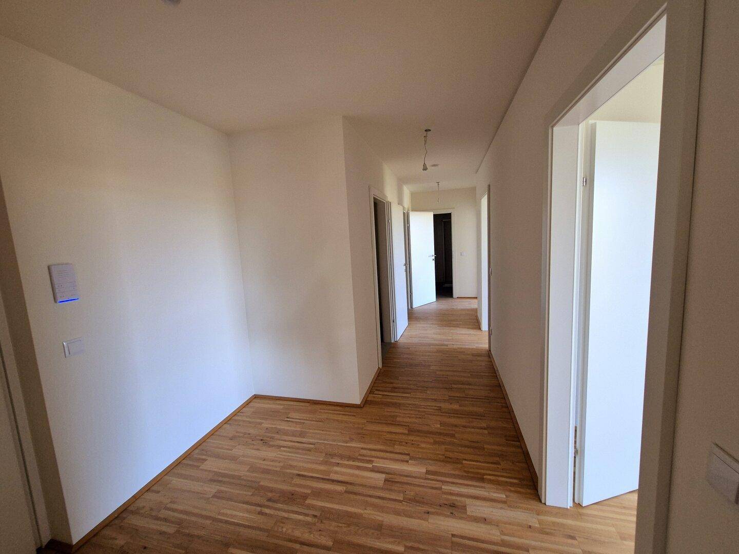 Heller Flur mit Parkettboden, weißen Wänden und mehreren Türen zu angrenzenden Zimmern.
