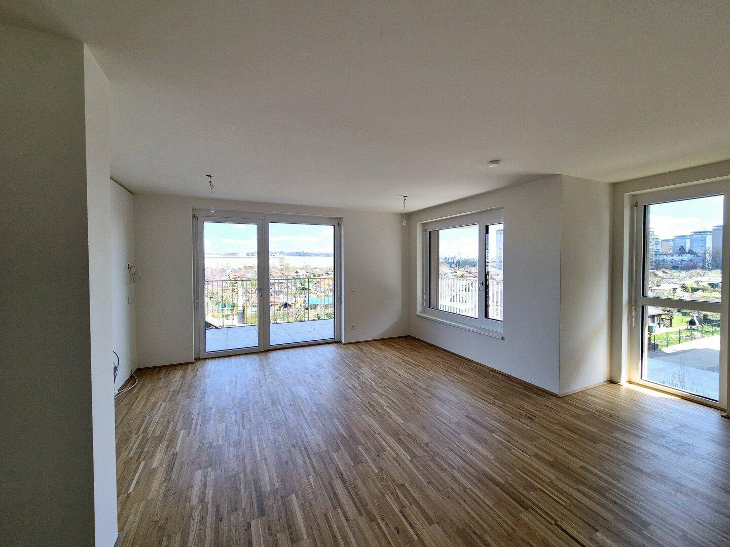 Helles, leeres Wohnzimmer mit Eichenparkettboden und großen Fenstern, die viel Tageslicht hereinlassen.