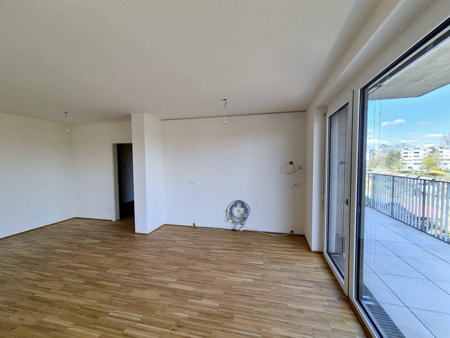 Geräumiges Wohnzimmer mit hellem Parkettboden und direktem Zugang zu einem großen Balkon.