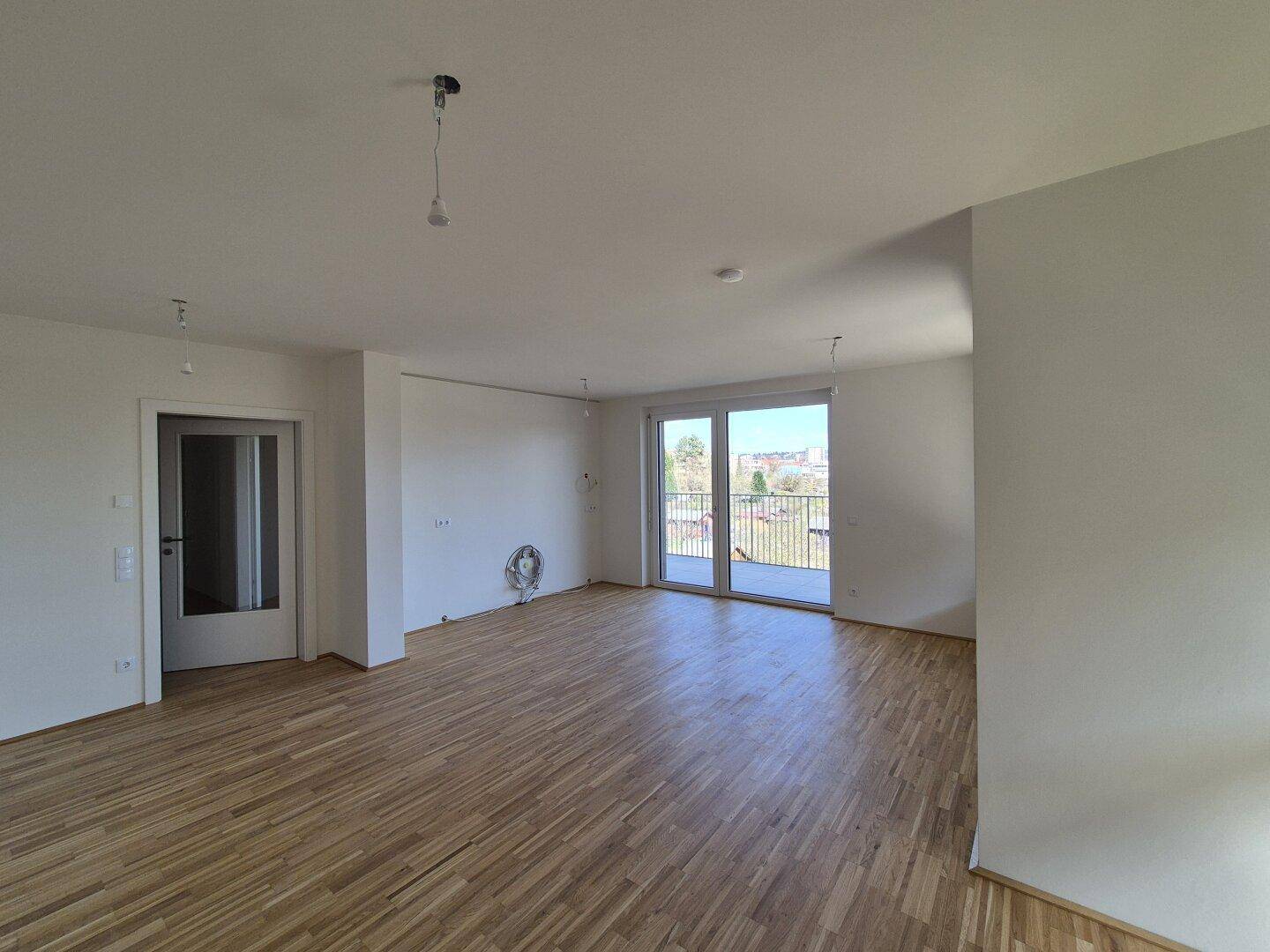 Großzügiges Wohnzimmer mit Holzboden und Zugang zu einem weiteren Raum sowie zum Außenbereich.