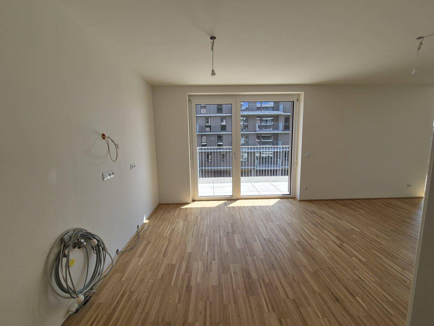 Geräumiges Wohnzimmer mit Parkettboden und Zugang zu einem Balkon, ideal für Entspannung.