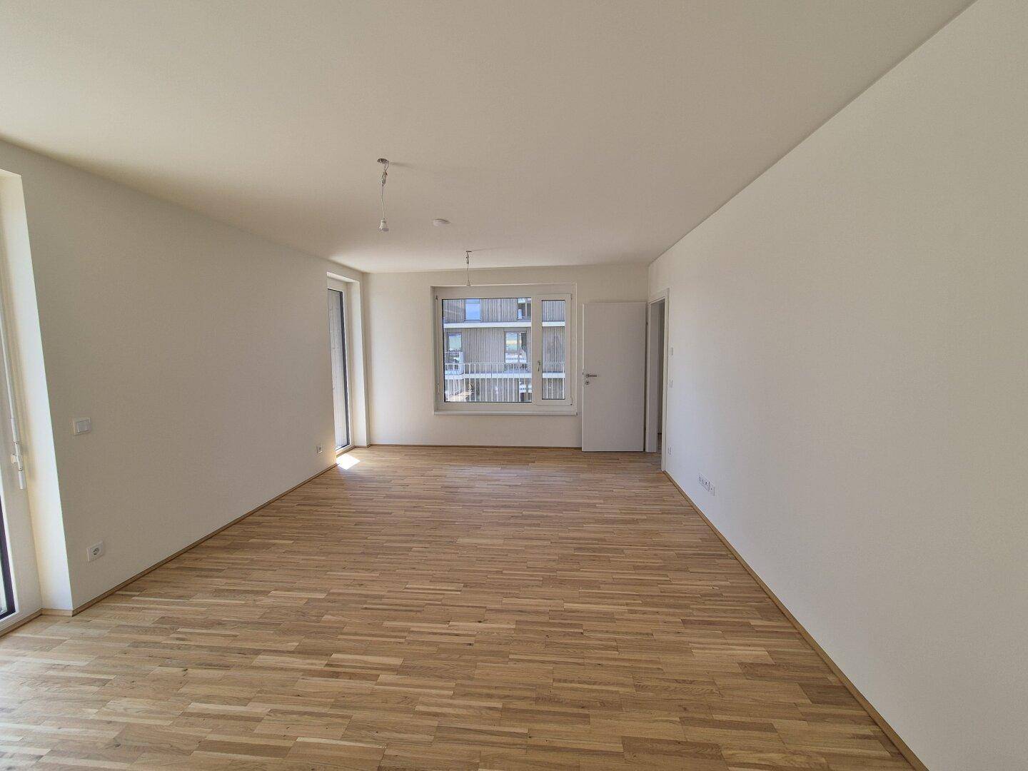 Langer, heller Raum mit Parkettboden und mehreren Fenstern, bereit zur individuellen Gestaltung.
