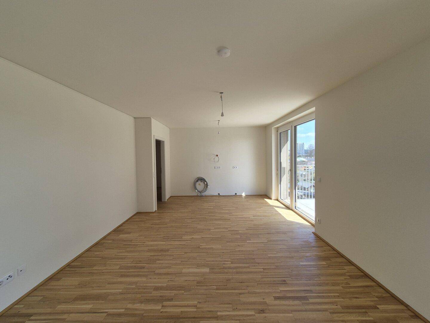 Helles Wohnzimmer mit Parkettboden und breitem Zugang zum Außenbereich, ideal für offenes Wohnen.