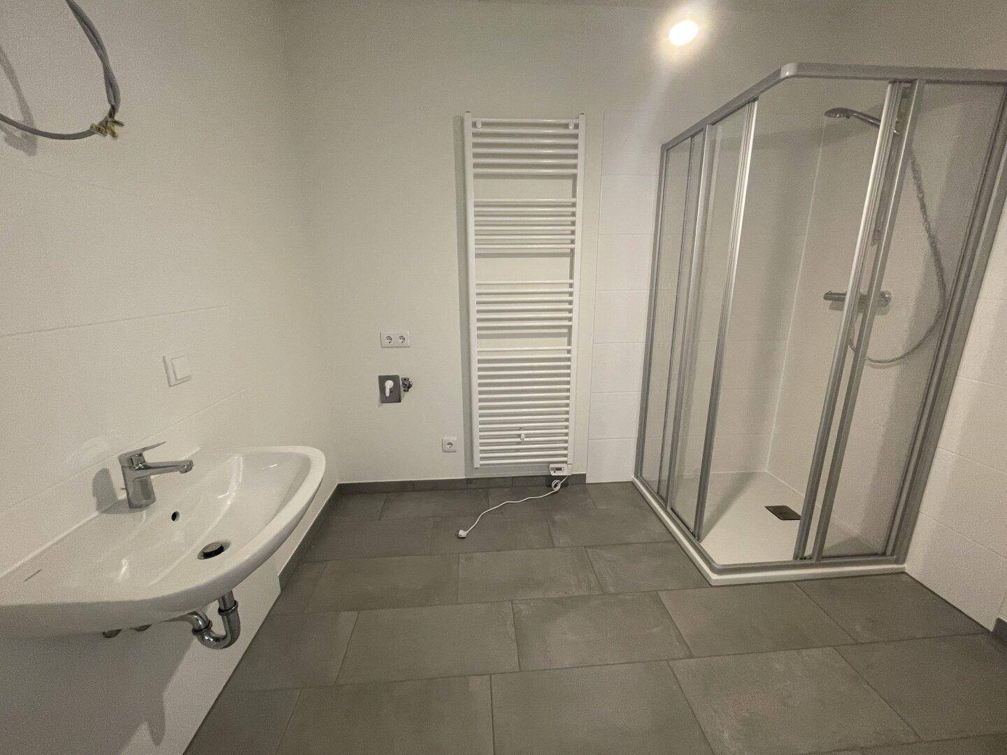 Modernes Badezimmer mit Dusche, Waschbecken und beheiztem Handtuchhalter, in dunklen Fliesen.