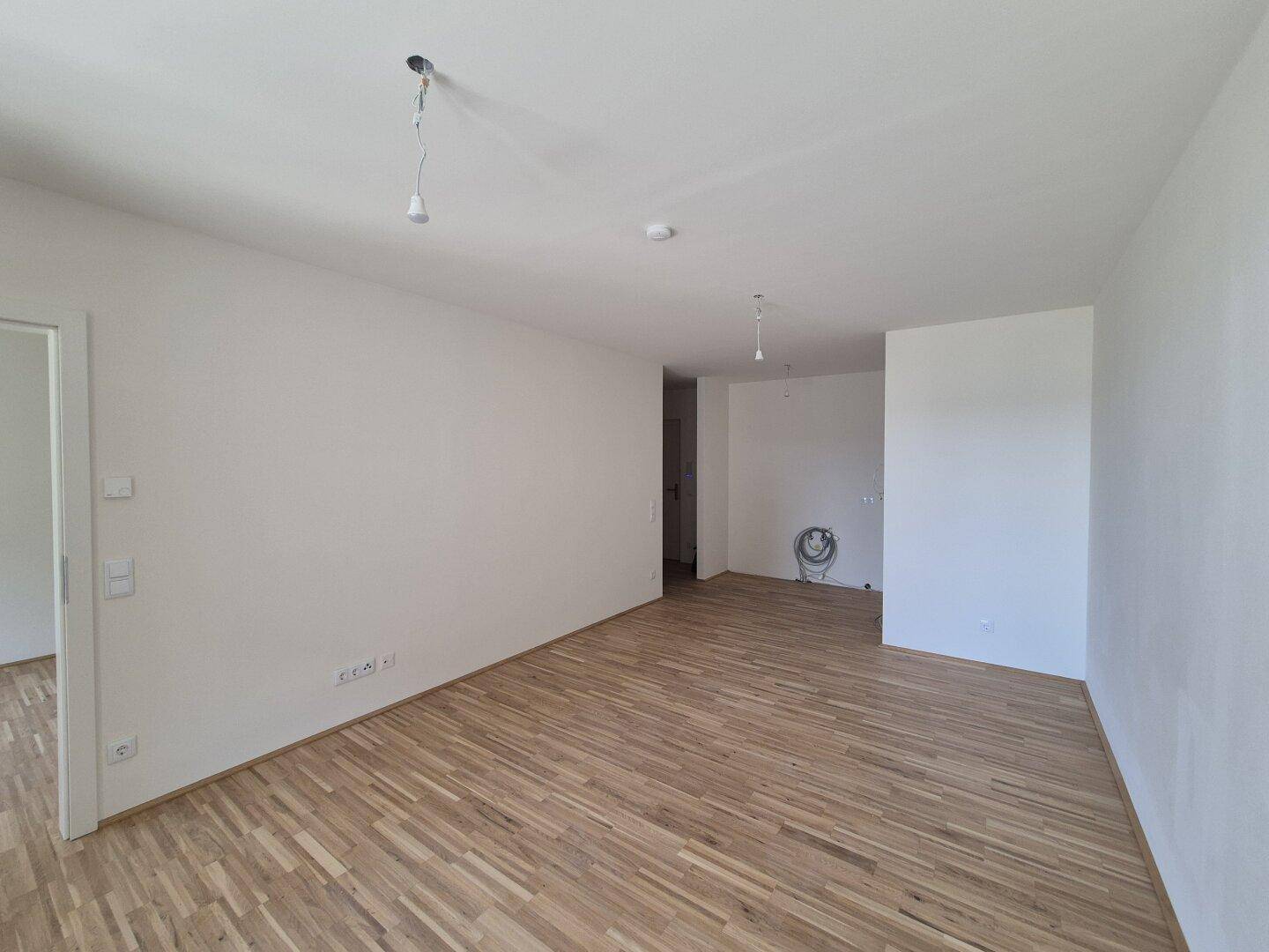 Heller, leerer Raum mit Holzparkettboden und weißen Wänden, bereit zur individuellen Gestaltung.