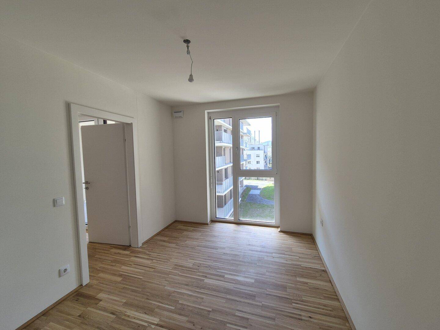 Helles Schlafzimmer mit Holzparkettboden und Zugang zu einem Außenbereich, ideal für Ruhe.