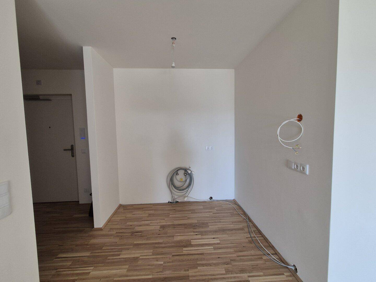 Unmöblierter Raum mit Holzparkettboden und vorbereiteten Anschlüssen für die weitere Einrichtung.