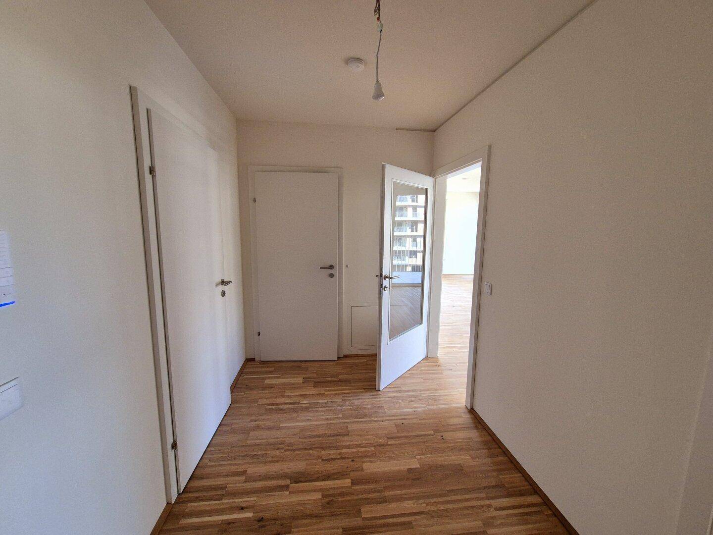 Heller Flur mit Holzparkettboden und weißen Türen, der zu weiteren Räumen führt.