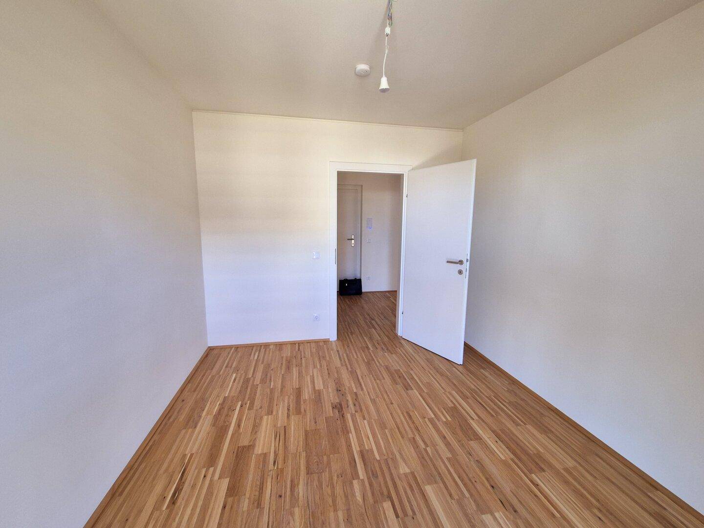 Leeres Schlafzimmer mit Holzparkettboden und weiß gestrichenen Wänden, bereit zum Einzug.