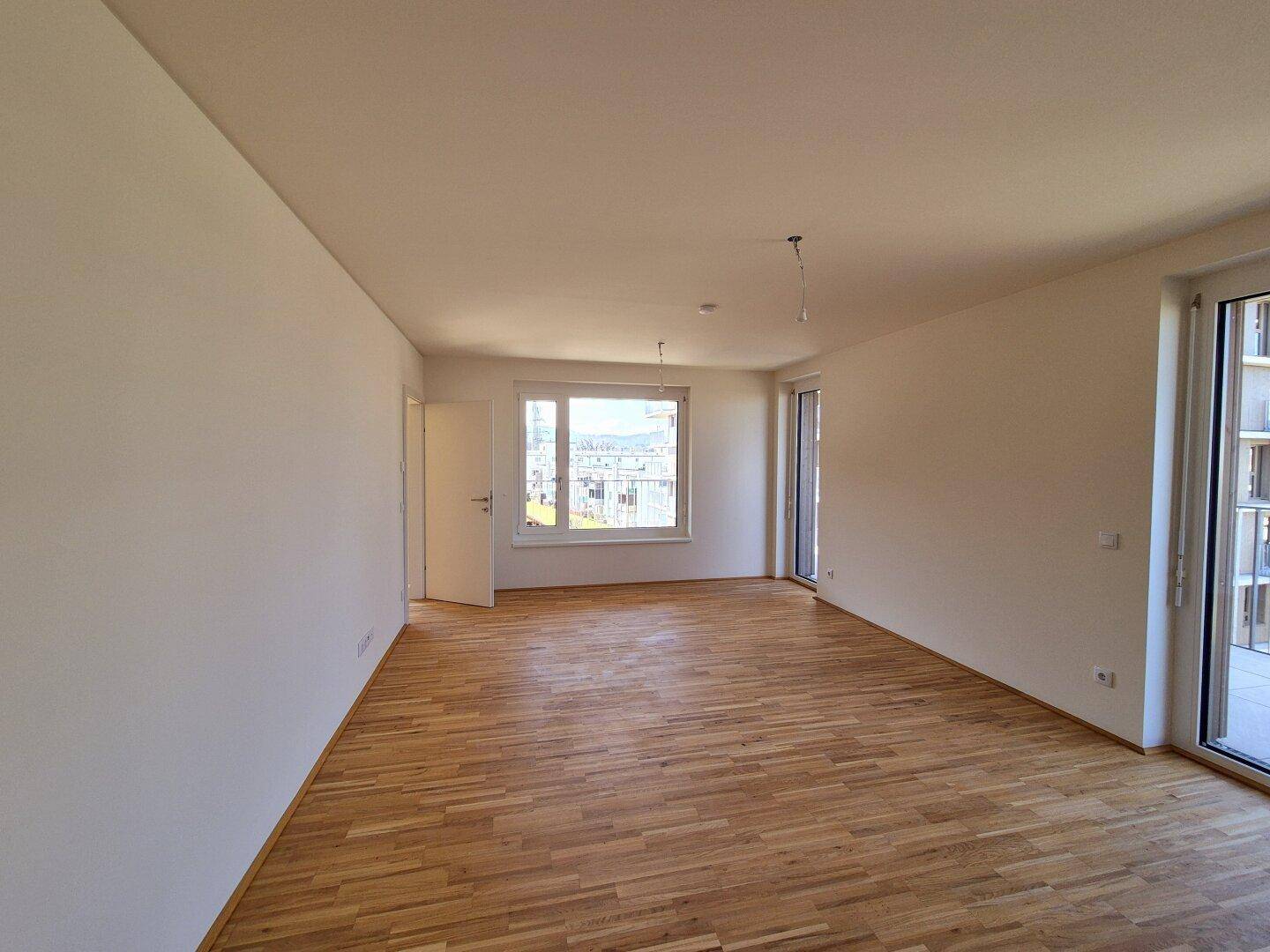 Heller Wohnbereich mit Holzparkettboden und großen Fenstern, die eine weite Aussicht bieten.