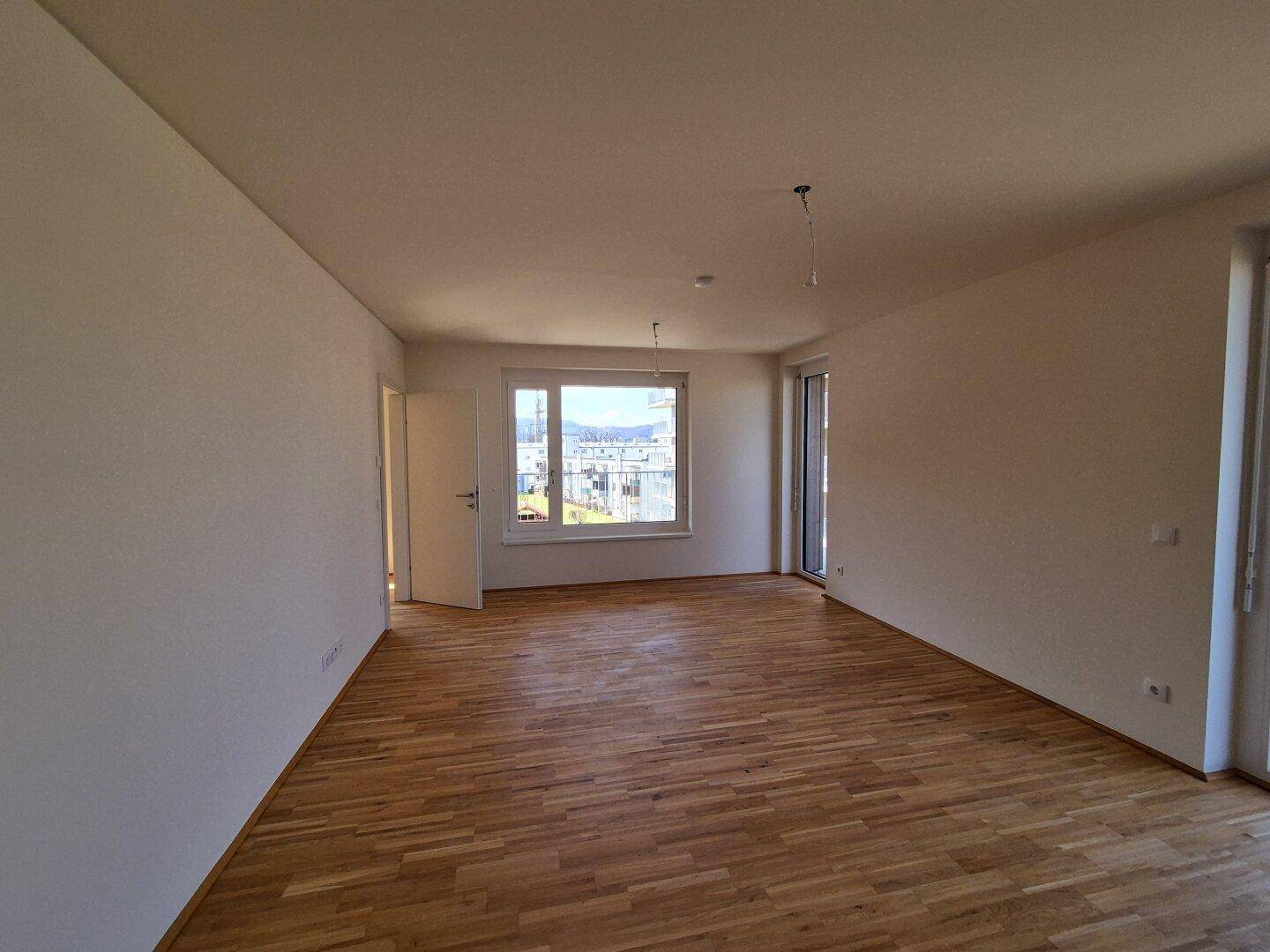 Großzügiger Wohnraum mit Holzparkettboden und hellen Wänden, ideal für individuelle Gestaltung.