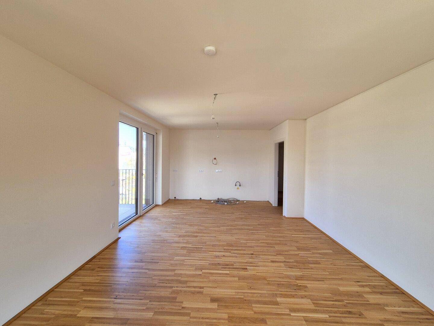 Offener Wohnbereich mit Holzparkettboden und Balkonzugang, ideal für eine moderne Wohnküche.